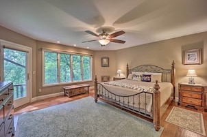 A bedroom with a large bed, a ceiling fan, a nightstand, a dresser, and a window with a view of trees.