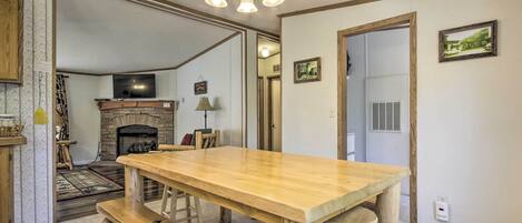 A spacious kitchen with a wooden table and benches, a fireplace, and a chandelier.