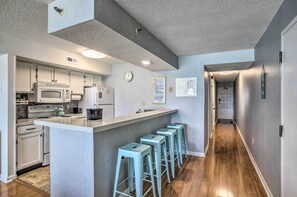 A modern kitchen with white cabinets, a central island, bar stools, and a wooden floor. - Oceanfront Condo w/ Pool in North Myrtle Beach (North Myrtle Beach)