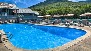 A swimming pool with lounge chairs and umbrellas, surrounded by a building with a mountain view. - Lincoln Condo w/ Amenities + Shuttle to Loon! (Lincoln)