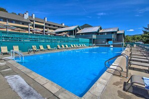 A swimming pool with lounge chairs and umbrellas, surrounded by a building with a view of a mountain.