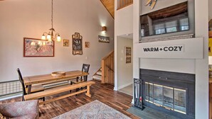 A cozy living room with a wooden dining table, benches, a fireplace, and a staircase leading to an upper level. - Lincoln Condo w/ Amenities + Shuttle to Loon! (Lincoln)
