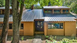 A two-story wooden house with a metal roof, a visible front door, and a pathway leading to the entrance. - Lincoln Condo w/ Amenities + Shuttle to Loon! (Lincoln)