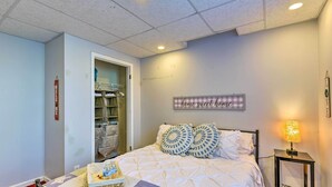 A bedroom with a bed, a bedside table with a lamp, a closet with hanging clothes, and a 'home sweet home' sign on the wall.