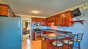 A kitchen with wooden cabinets, a built-in microwave, a refrigerator, and a bar area with stools.