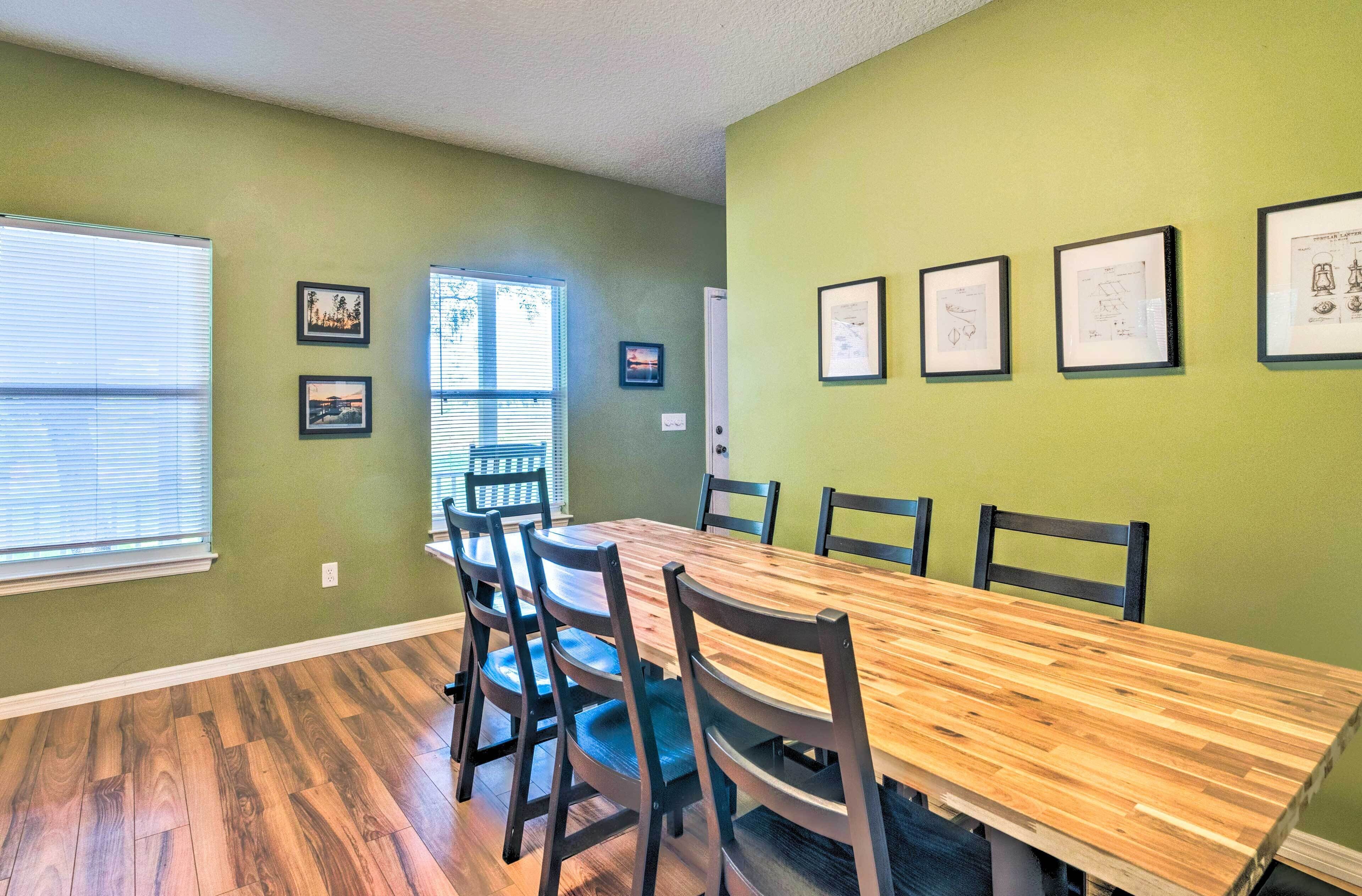 A dining room with a wooden table and chairs, green walls, and framed pictures on the wall.