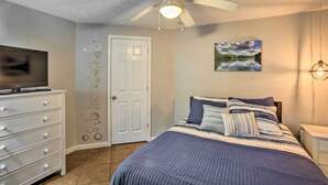 Une chambre à coucher avec un lit, un ventilateur de plafond, une télévision, une commode et une porte.