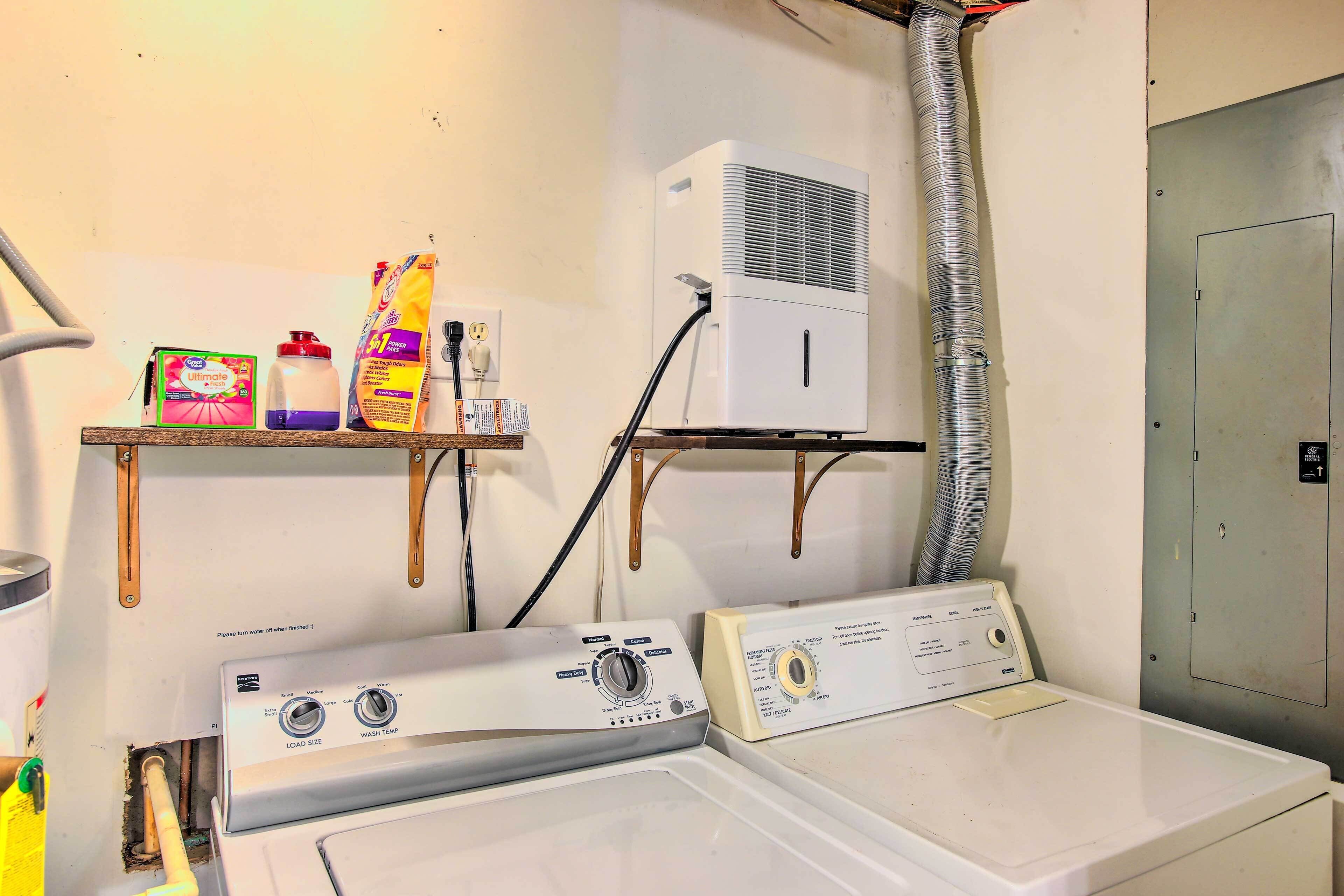 A laundry area with two washers and dryers, a shelf with cleaning supplies, and an air conditioning unit.