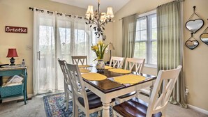 A dining room with a wooden table, white chairs, a chandelier, and a vase with flowers. - Bring a Pet: Cozy Burnsville Cottage w/ Fire Pit! (Burnsville)