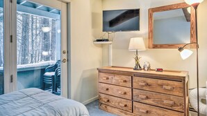 Une chambre à coucher avec un lit, une commode en bois, une télévision, un miroir et un balcon avec des chaises.