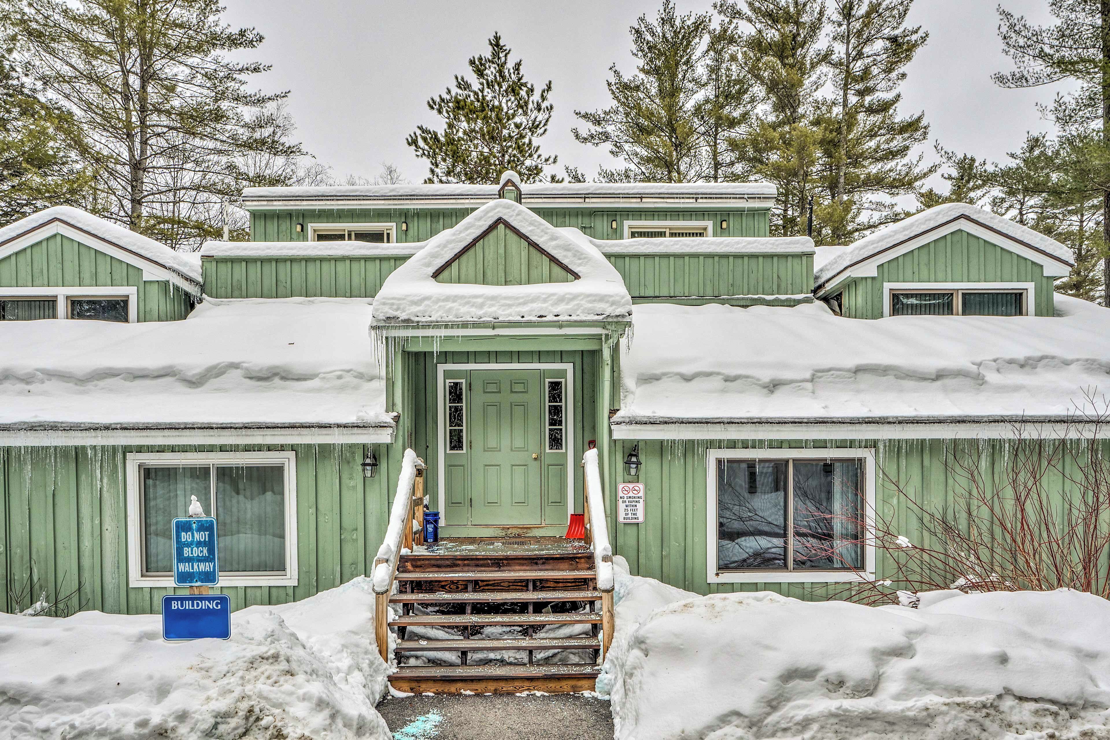 A green building with a snow-covered entrance and steps leading up to the door.