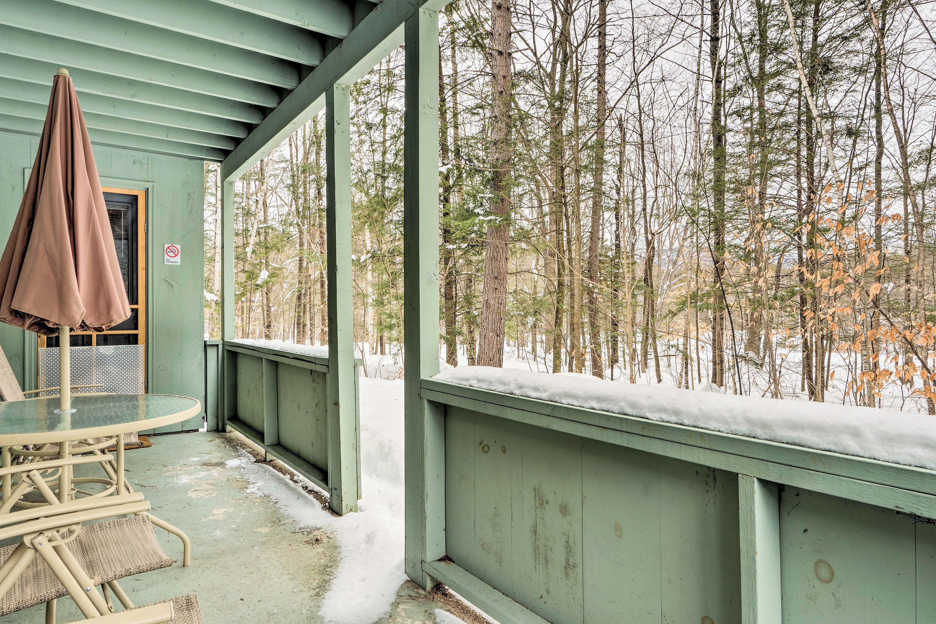 A covered outdoor seating area with a table and chairs, a bench, and a view of a snowy forest.