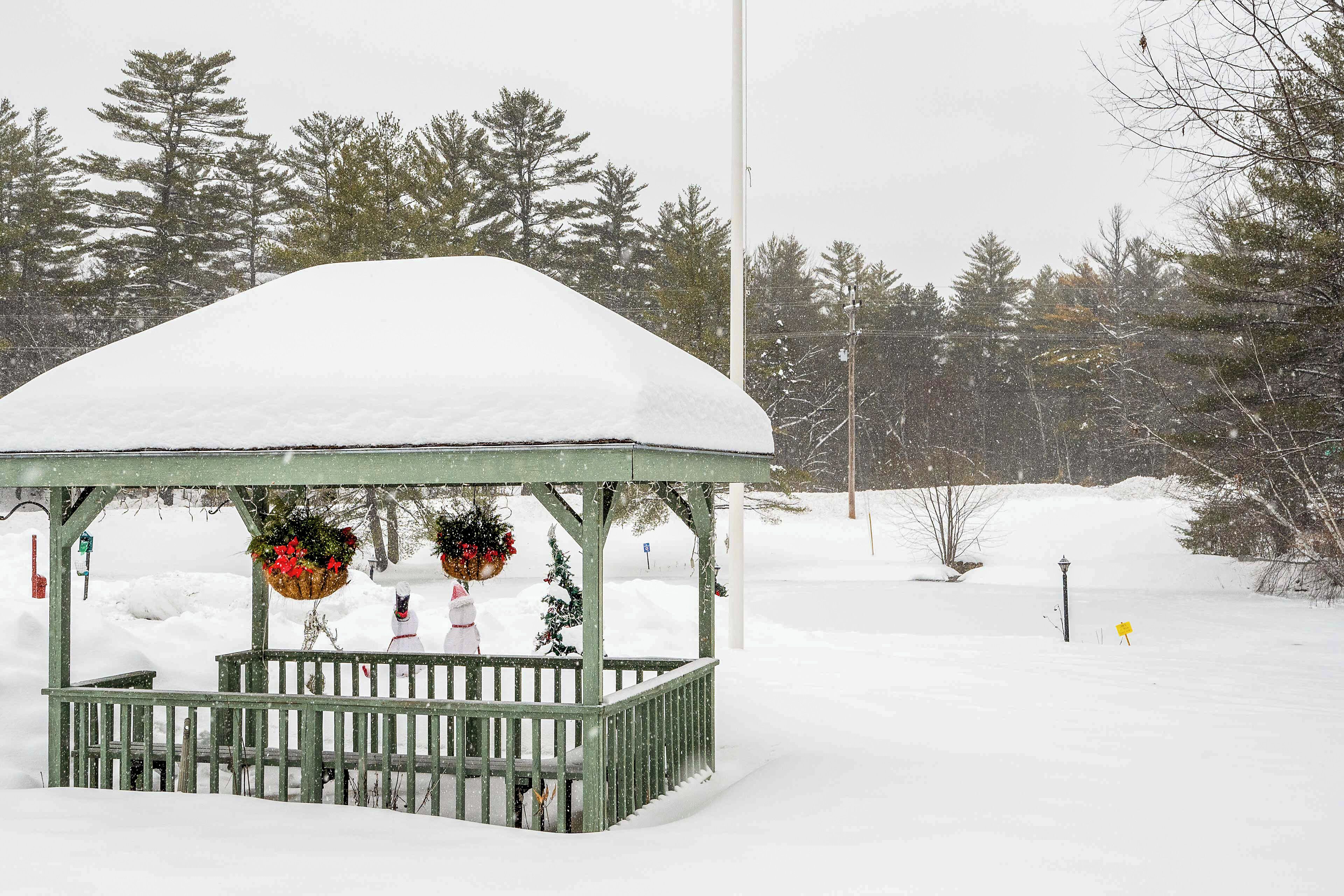 A gazebo covered in snow with a bench and hanging decorations.