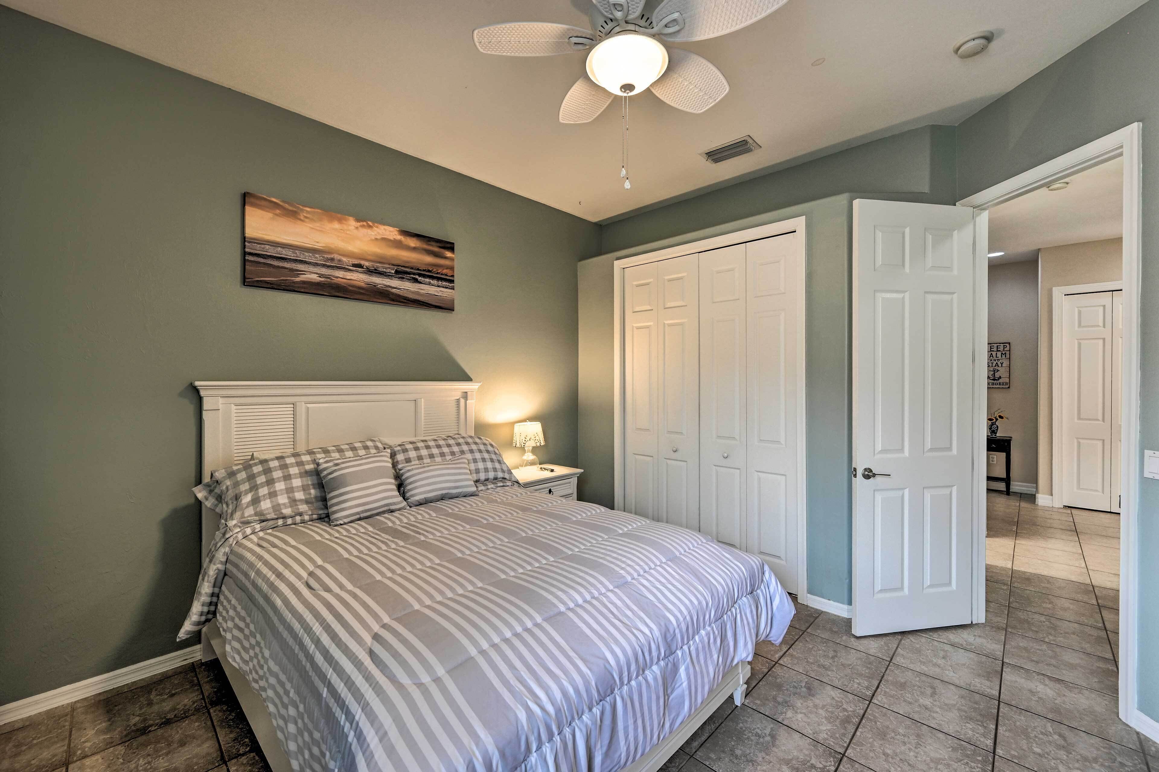 A bedroom with a bed, a ceiling fan, a nightstand, and a painting on the wall.