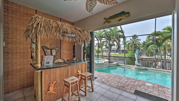 A tiki bar with a thatched roof, a pool with a fountain, and a view of palm trees.