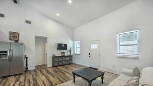 A spacious living room with a wooden floor, a dark wooden coffee table, a white sofa, and a flat-screen TV mounted on the wall. - Rural Gilmer House w/ Covered Patio! (Gilmer)