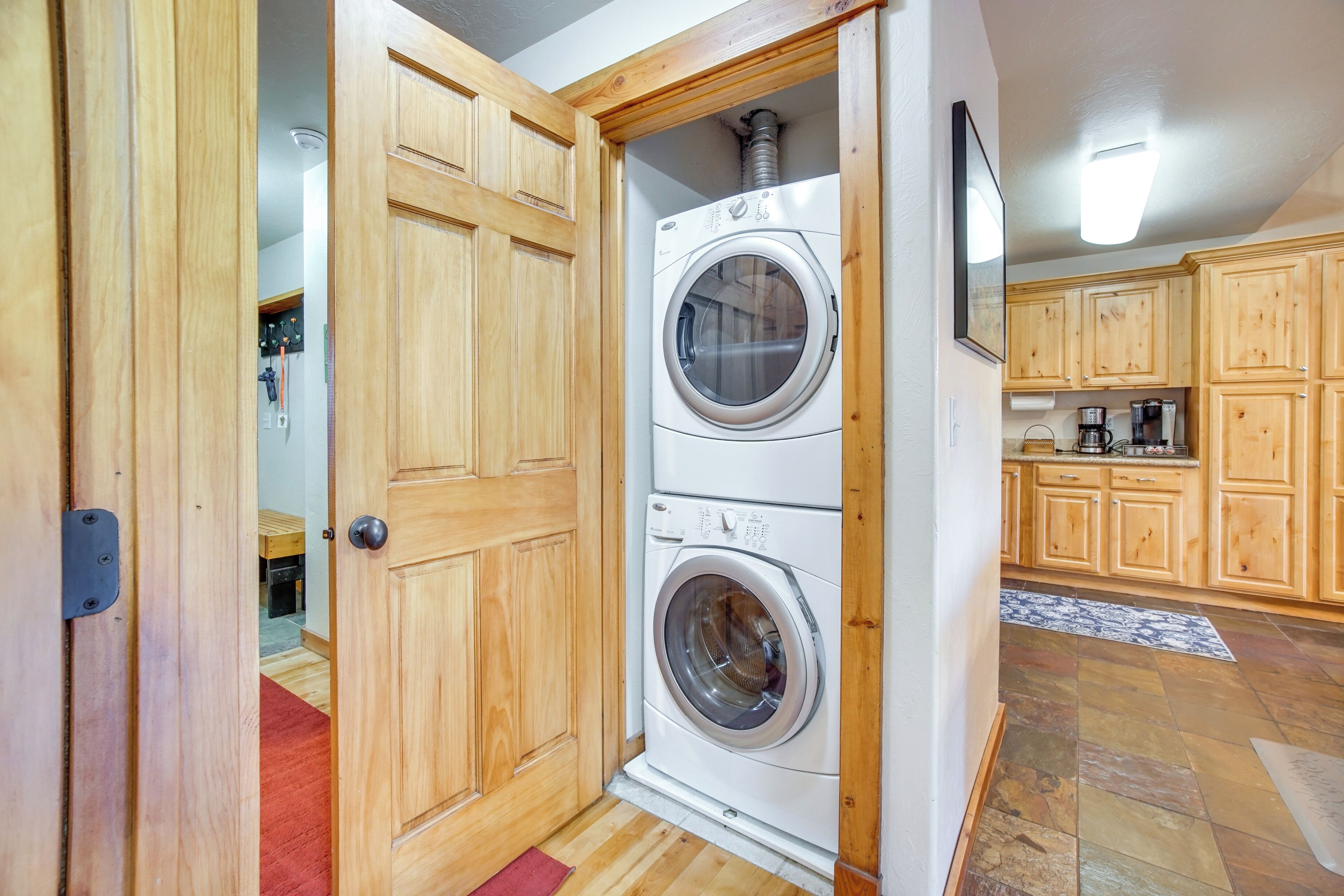 A laundry area with two stacked washing machines, wooden cabinets, and a kitchen area with a coffee maker.