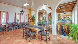 A spacious dining area with a long wooden table and chairs, surrounded by arches and potted plants. - Los Cerrillos Hillside Hacienda on 65 Acres! (Cerrillos)