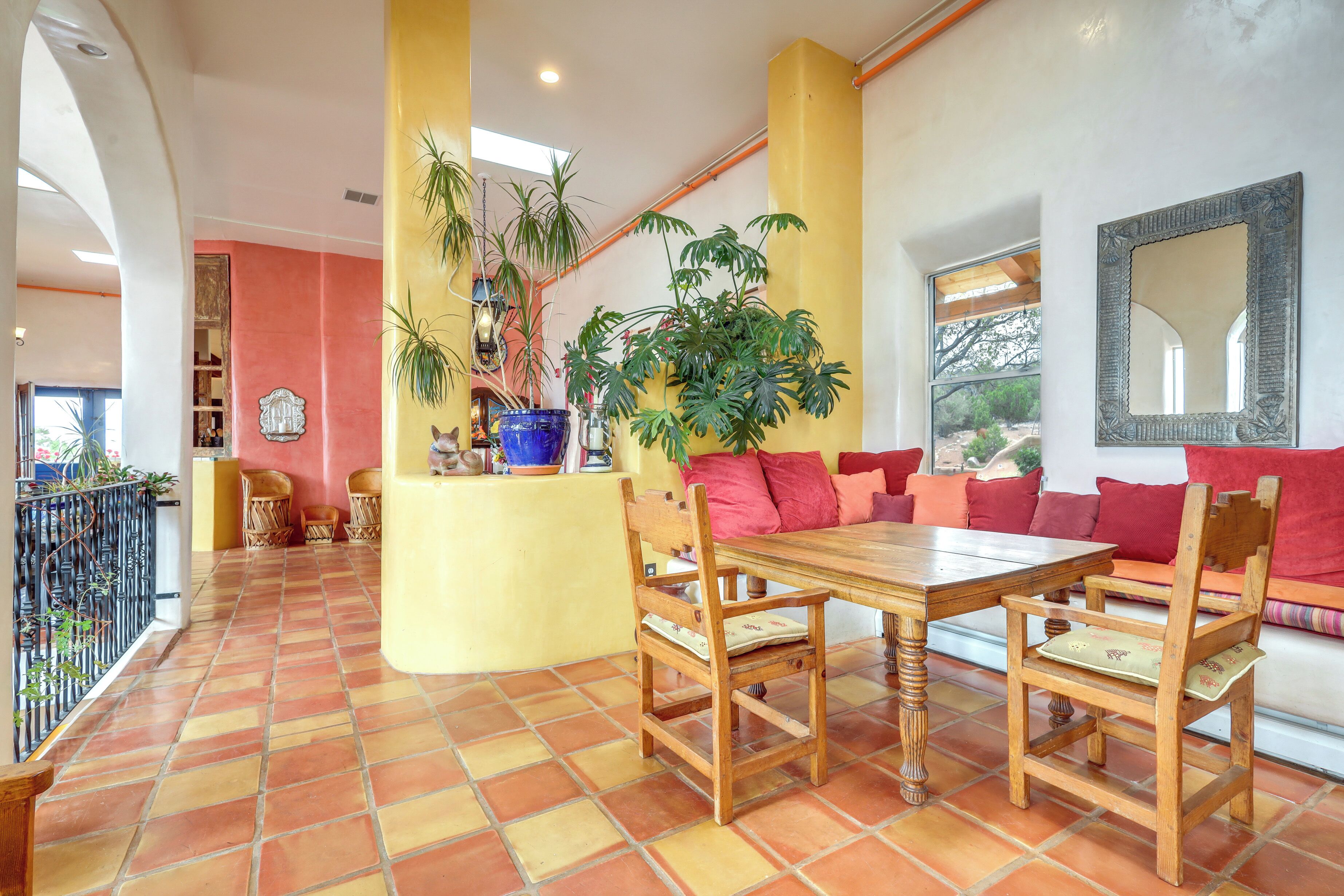 A dining area with a wooden table and chairs, a yellow pillar, and a red sofa.