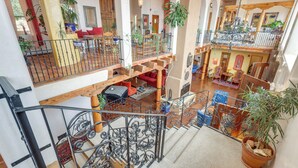 A spacious interior with a staircase, multiple seating areas, and various potted plants. - Los Cerrillos Hillside Hacienda on 65 Acres! (Cerrillos)