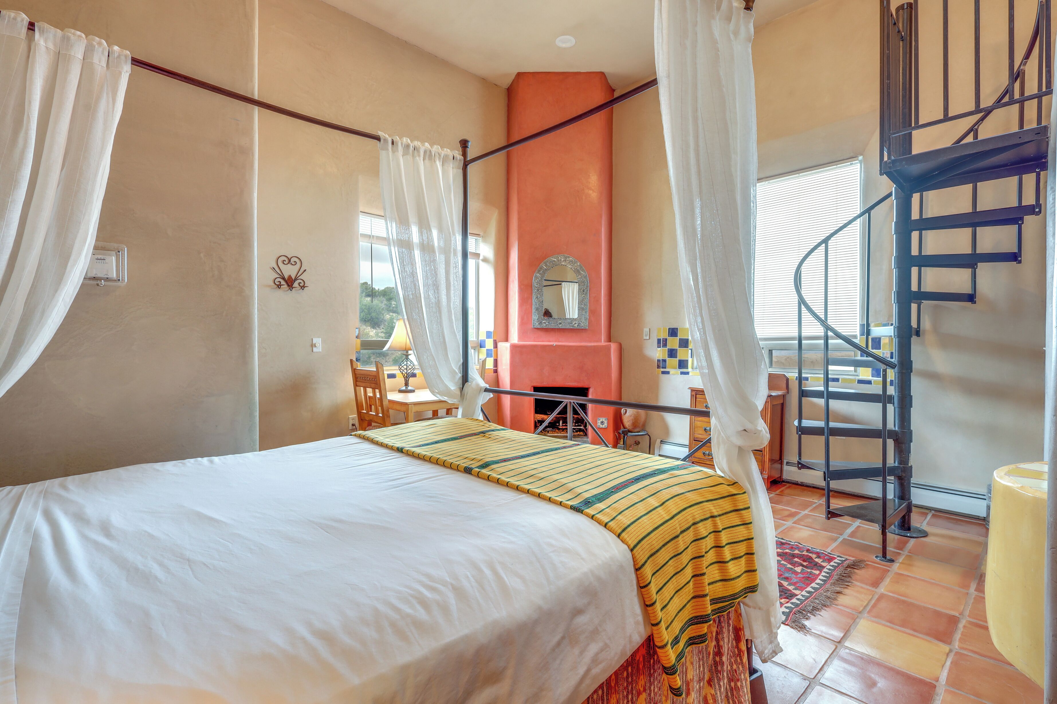 A bedroom with a bed, a fireplace, a staircase, and a window.