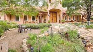 A courtyard with a patio, outdoor seating, and a building with a tiled roof and arched doorways. - Los Cerrillos Hillside Hacienda on 65 Acres! (Cerrillos)