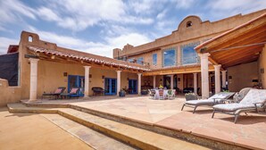 A spacious courtyard with outdoor seating, a covered patio, and a large building with multiple windows and doors. - Los Cerrillos Hillside Hacienda on 65 Acres! (Cerrillos)