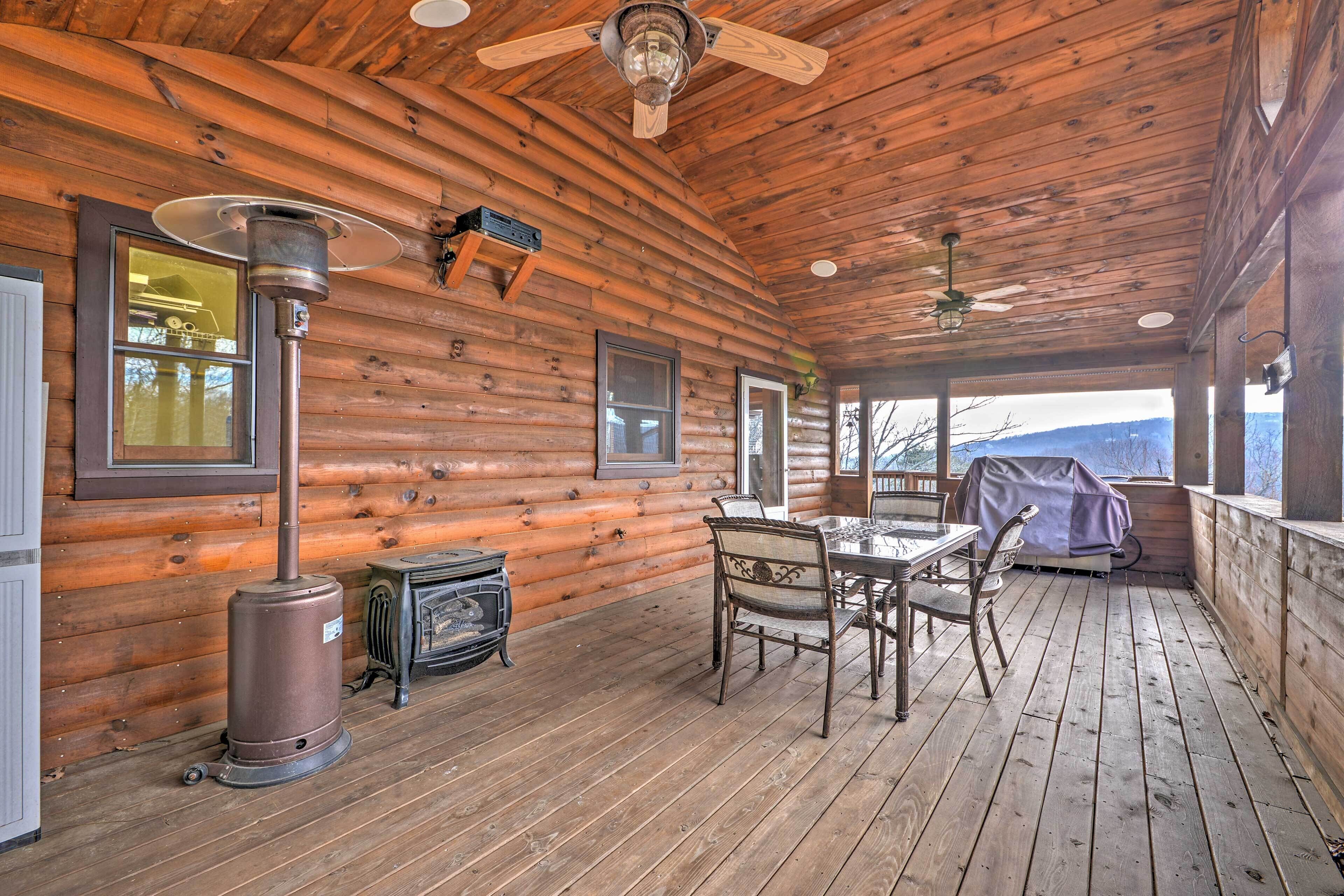 A wooden cabin with a covered porch, a table with chairs, a heater, and a fireplace.