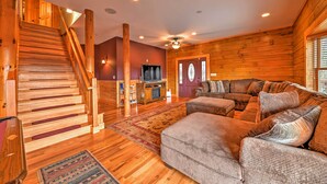Un intérieur en bois avec un escalier, un salon avec un canapé et des coussins, et un téléviseur.