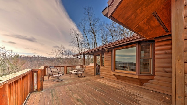 Une terrasse en bois avec des meubles d’extérieur, une grande fenêtre et une vue sur les arbres et les montagnes.