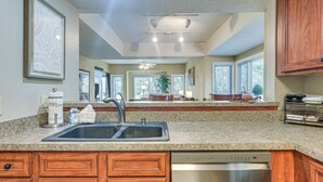 A kitchen with granite countertops, wooden cabinets, a stainless steel dishwasher, and a large window providing natural light. - Golf Course Home w/ Balcony in North Myrtle Beach! (North Myrtle Beach)