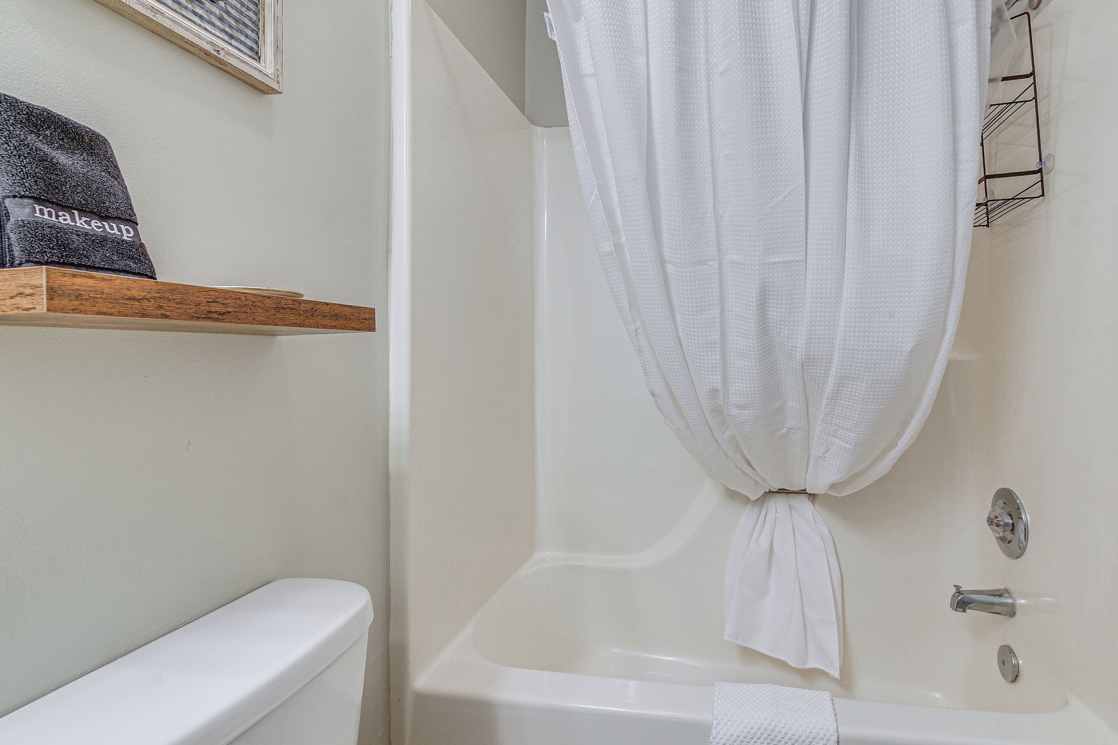 A bathroom with a white bathtub, a wooden shelf with a towel, and a white curtain tied at the top.