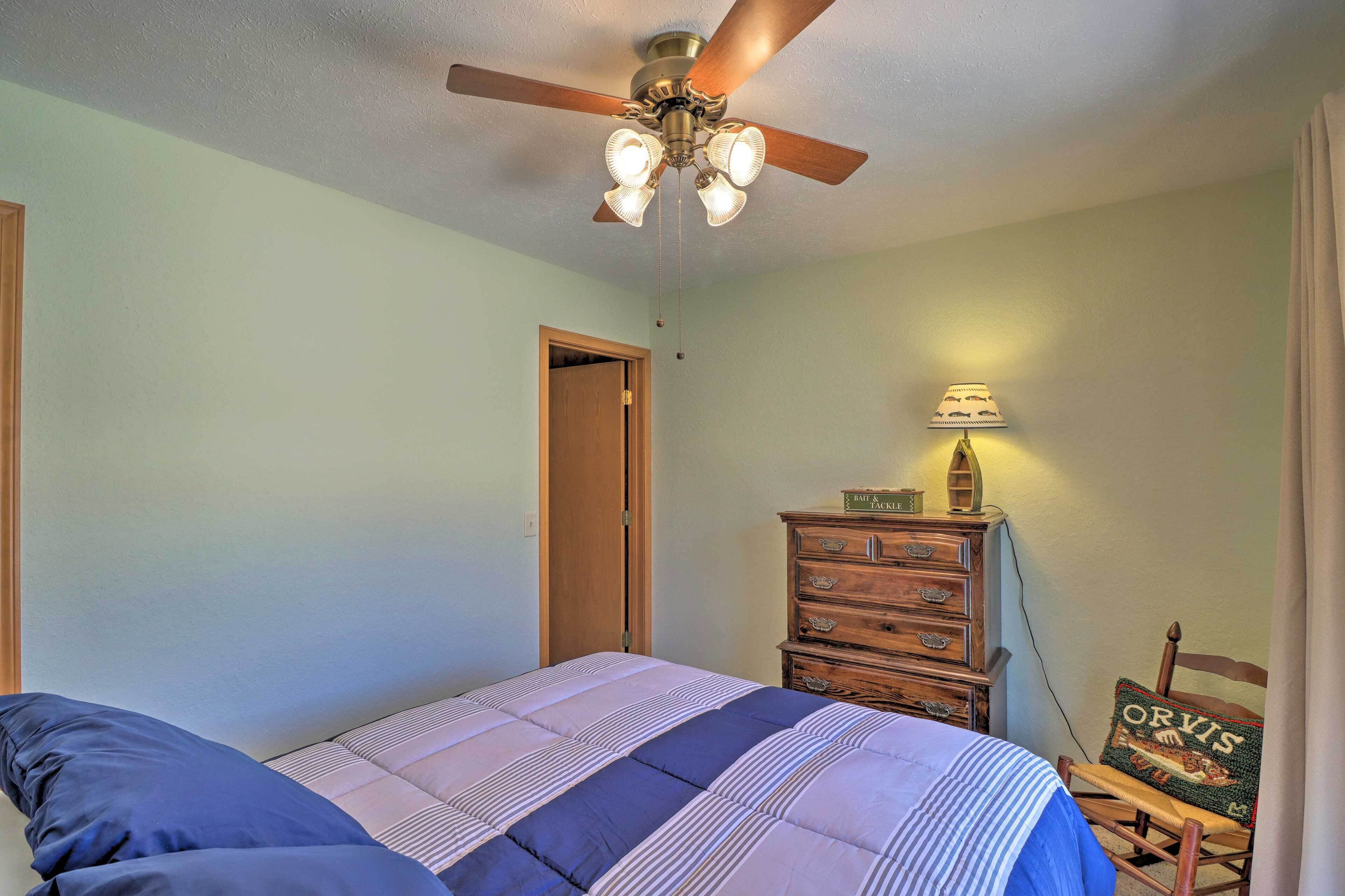 A bedroom with a bed, a wooden dresser, a ceiling fan, and a door.