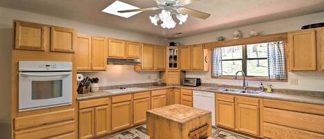A kitchen with wooden cabinets, a ceiling fan, a microwave, and a window with curtains.