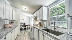 A kitchen with white cabinets, granite countertops, a stainless steel sink, and a window with a view of greenery. - Tranquil Creekfront Bryson City Home w/ Grill! (Bryson City)