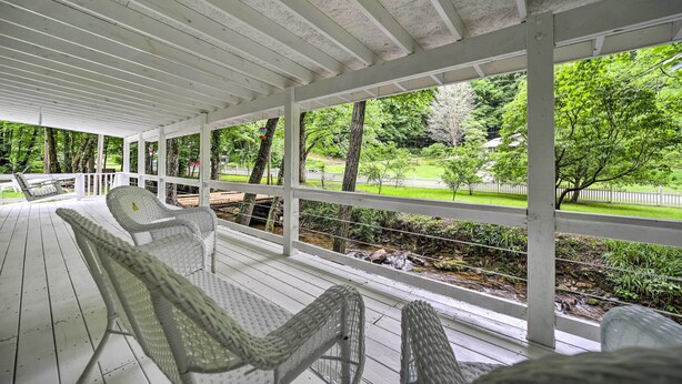 A covered outdoor seating area with wicker chairs and a view of a landscaped garden. - Tranquil Creekfront Bryson City Home w/ Grill! (Bryson City)