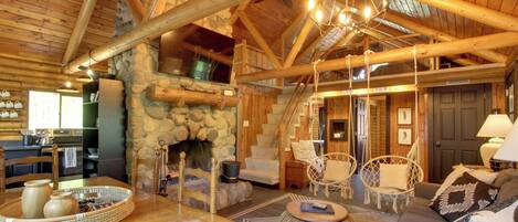 A cozy log cabin interior with a stone fireplace, wooden furniture, and a dining area.