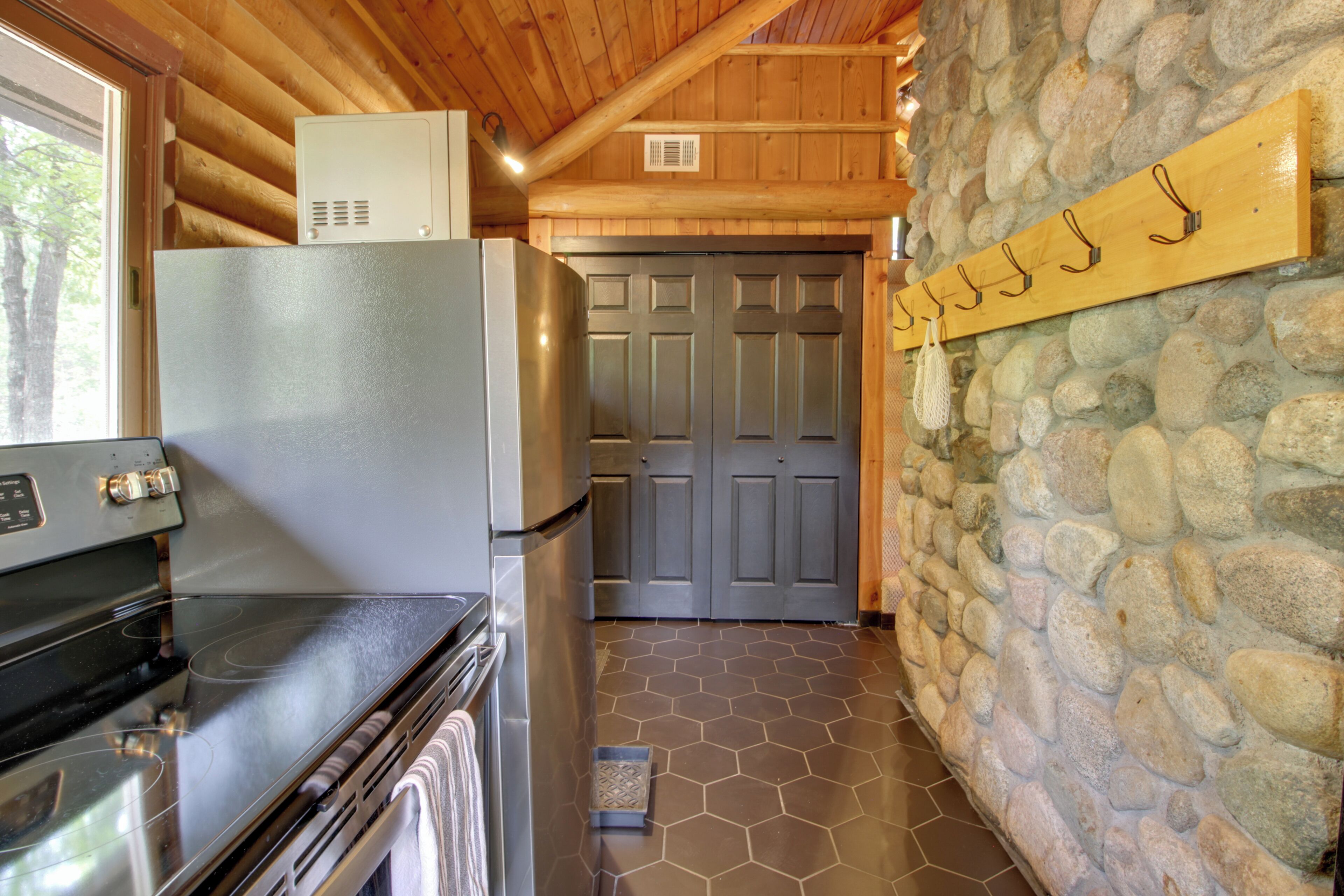 A kitchen with a refrigerator, stove, and stone wall.