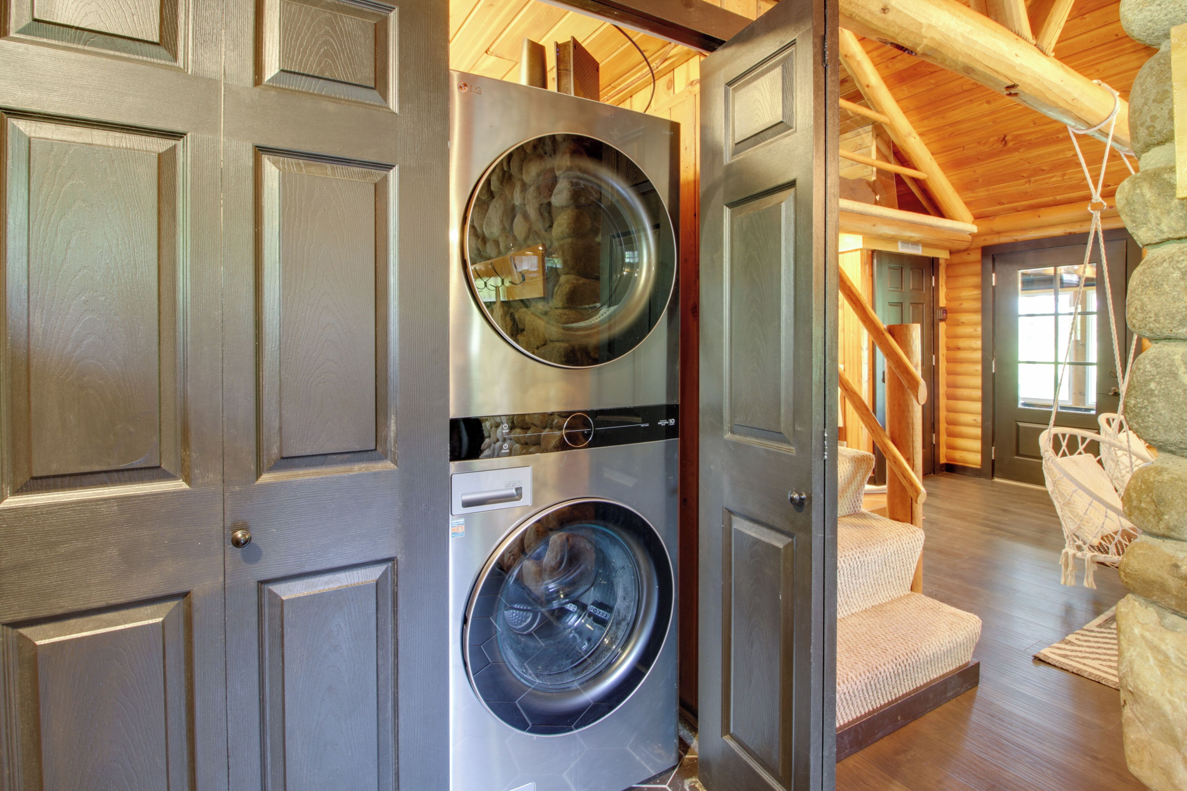 A laundry room with a front-loading washer and dryer, wooden interior, and a stone wall.