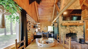Ein Holzblockhaus-Innenraum mit Kamin aus Stein, Holzesstisch und einer hängenden Pflanze.