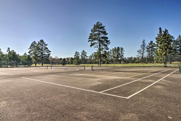 Ein Außen-Tennisplatz mit blauem Himmel und Bäumen im Hintergrund.