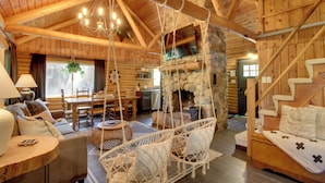 Ein Interieur einer Blockhütte mit Kamin aus Stein, Holzmöbeln und einem Hängesessel.