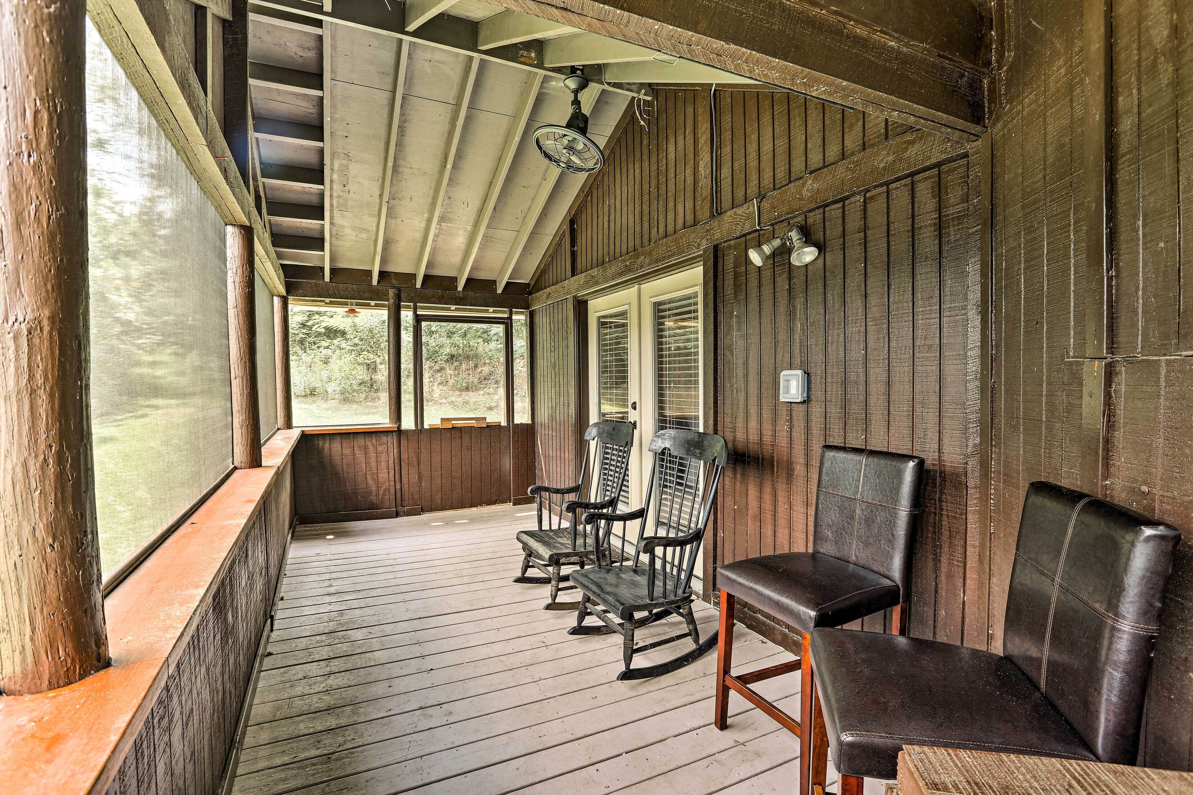 A wooden porch with rocking chairs and a table, overlooking a natural landscape.