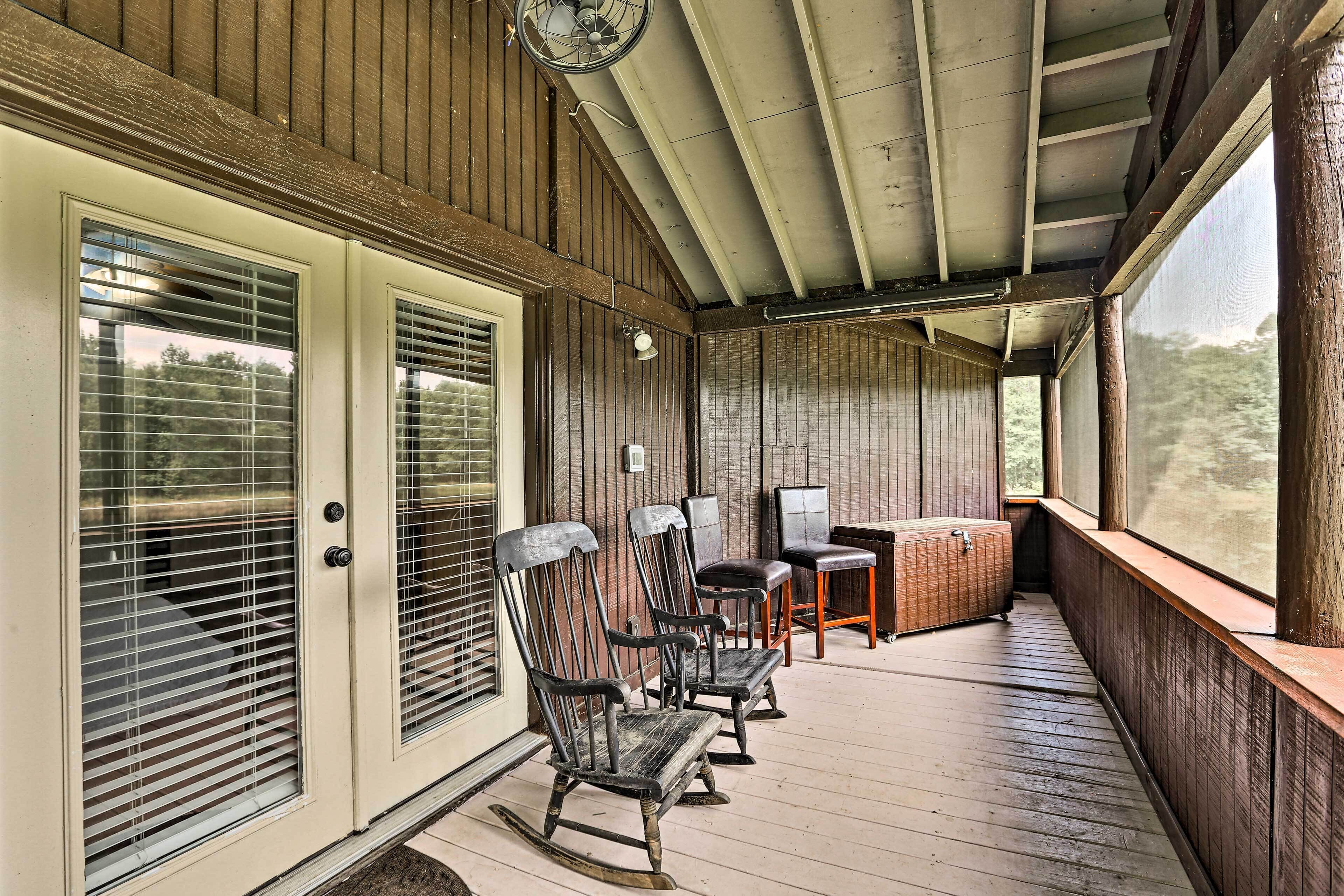 A covered porch with wooden flooring, a seating area with chairs and a table, and a view of the outdoors.