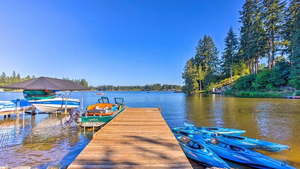 A wooden dock with boats and kayaks, a clear blue sky, and a forested hillside. - Lakeside Lacey Gem w/ Fire Pit + Private Dock (Lacey)