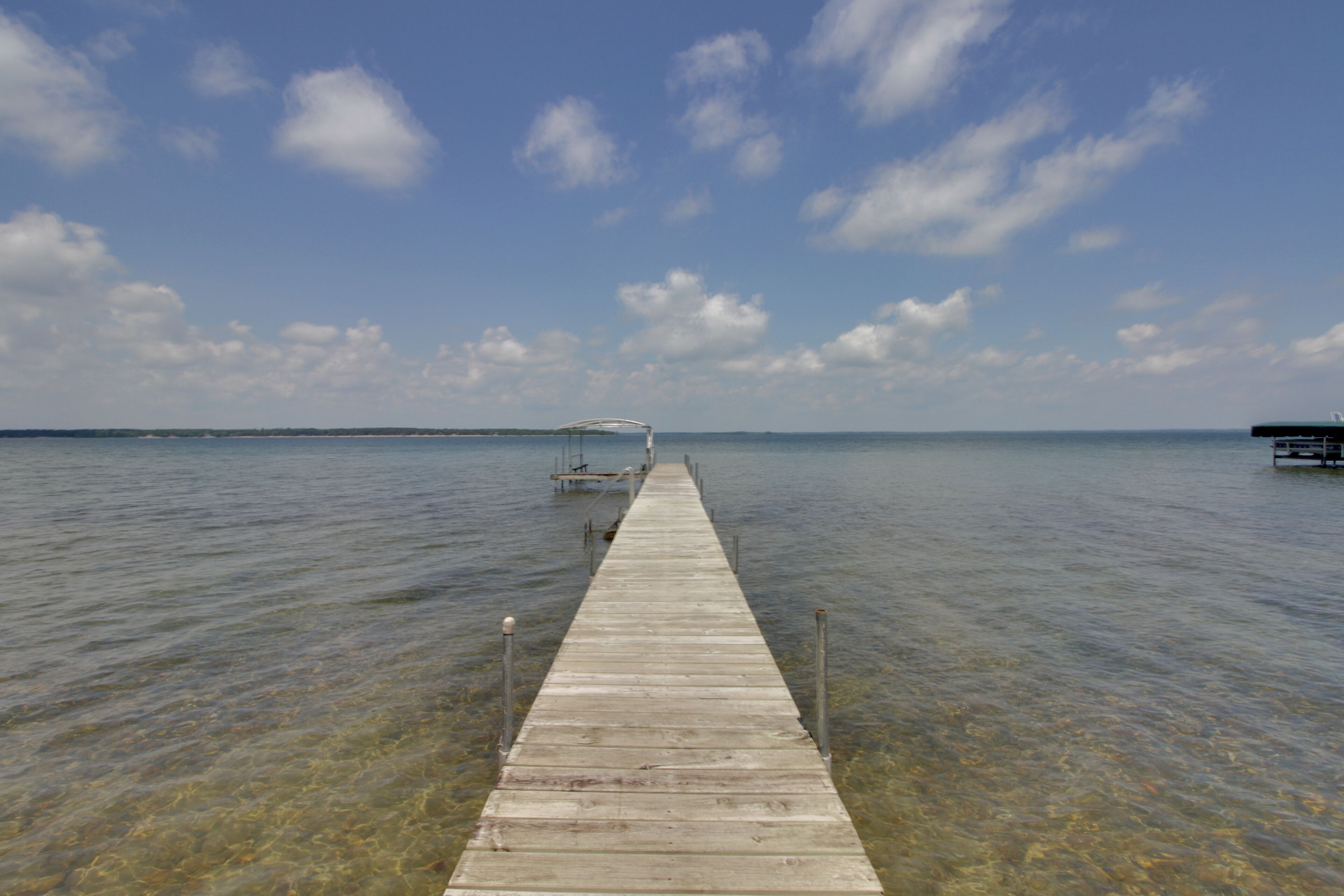 A wooden pier extending into calm water under a clear sky.