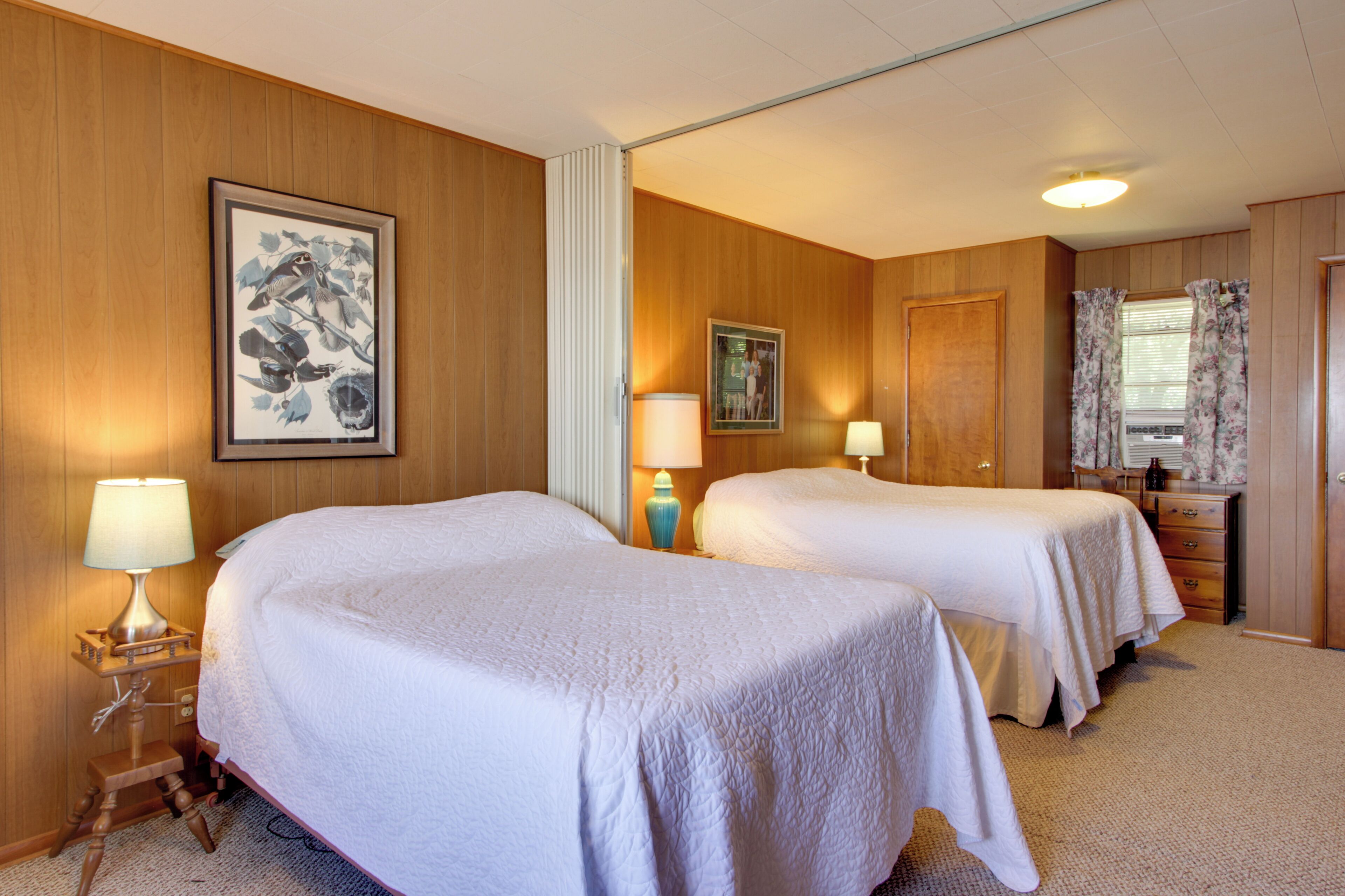 A hotel room with two beds, wooden paneling, framed artwork, and a dresser with a mirror.