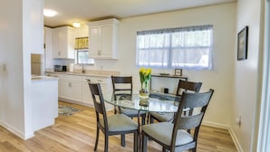 A dining area with a glass table surrounded by four chairs, a vase with yellow flowers, and a window with sheer curtains. - Renovated Crescent Lake Escape w/ Waterfront Deck! (Crescent City)