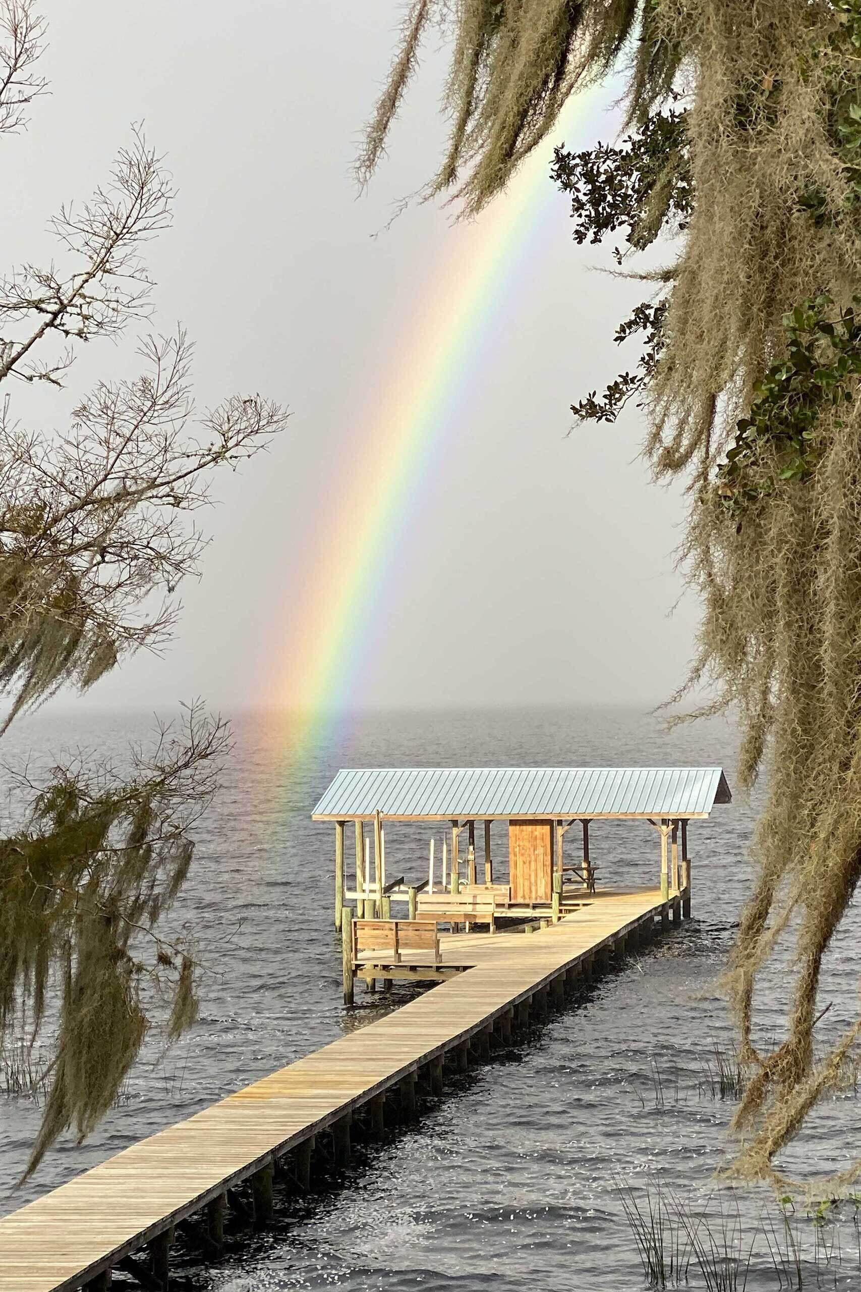 A wooden pier leading to a small wooden structure with a metal roof, surrounded by water and trees.