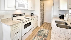 A kitchen with white cabinets, a stove, a microwave, a coffee maker, and a sink. - Renovated Crescent Lake Escape w/ Waterfront Deck! (Crescent City)